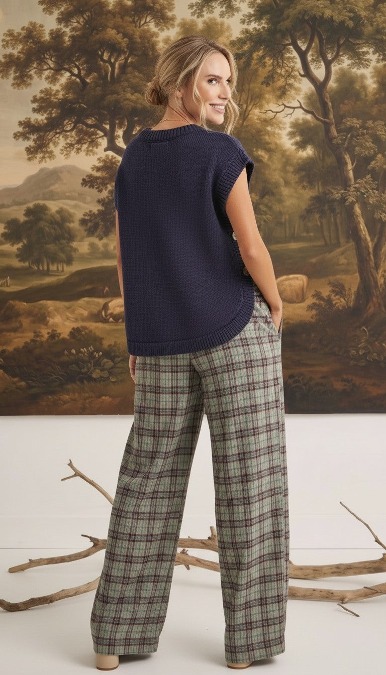 graced navy crew neck sweater vest with side buttons worn by a model with plaid trousers in a studio setting