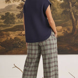 graced navy crew neck sweater vest with side buttons worn by a model with plaid trousers in a studio setting