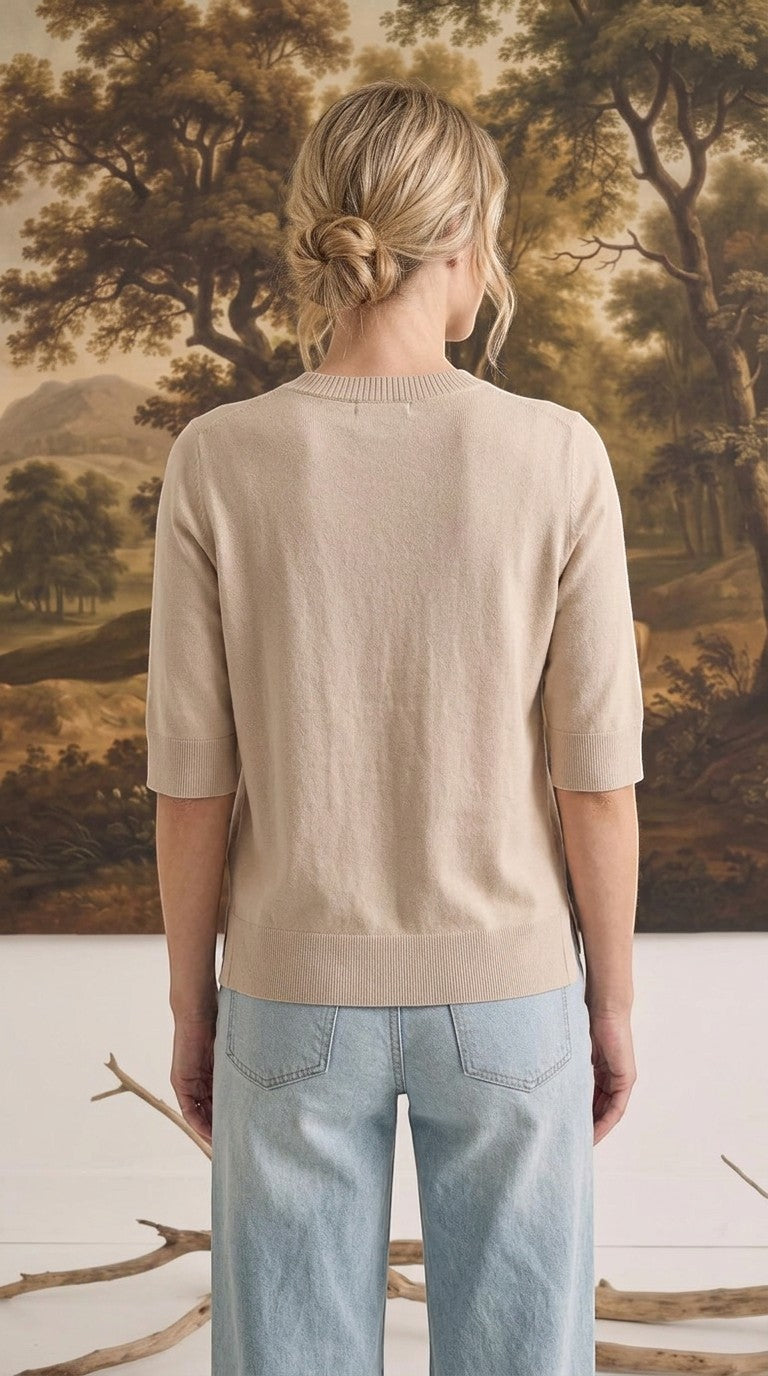 Back view of a woman wearing a graced oatmeal short sleeve knit top with a ribbed crew neck and hem
