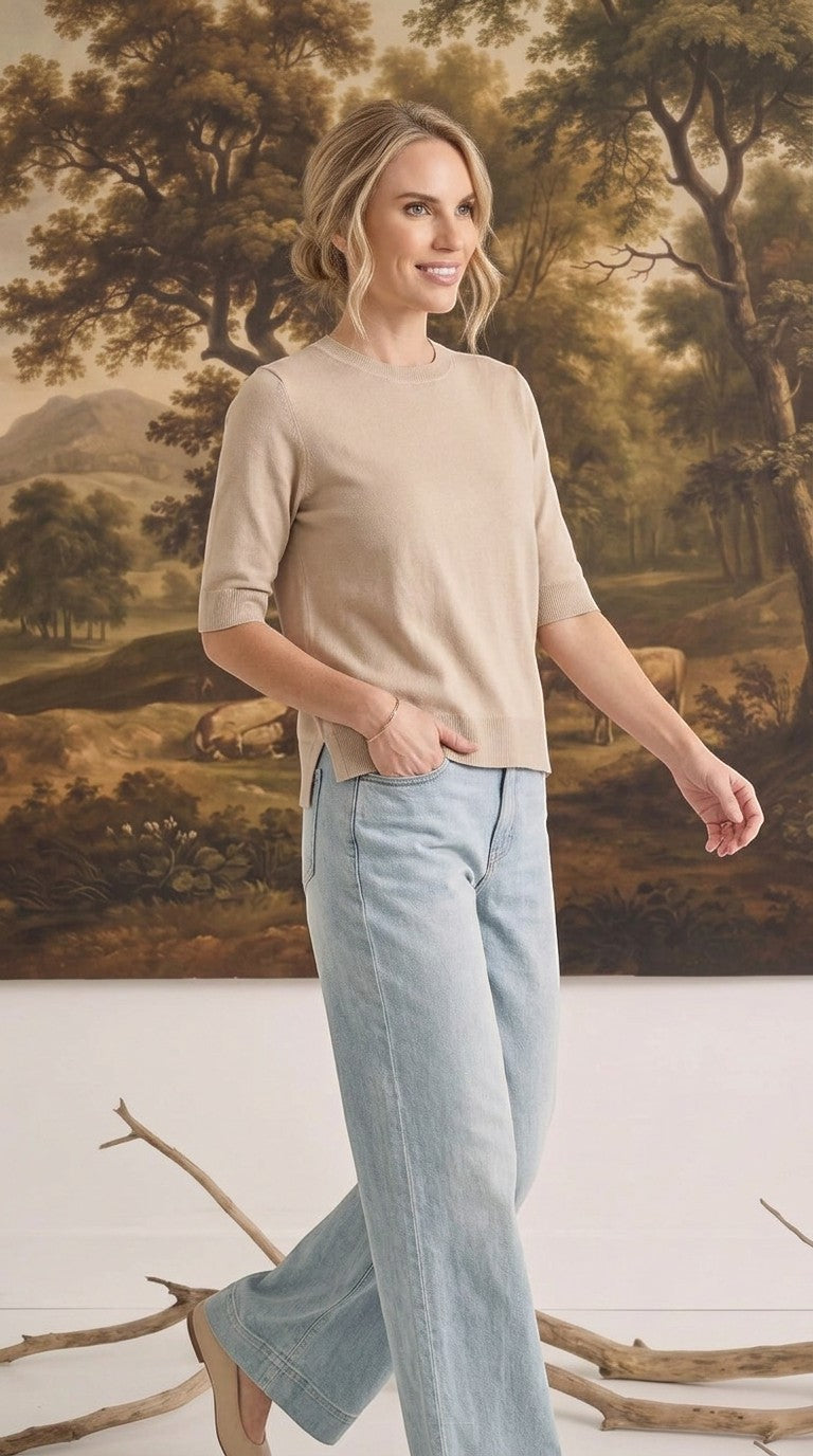 Model wearing a graced oatmeal short sleeve knit top with light wash jeans in a studio setting