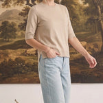 Model wearing a graced oatmeal short sleeve knit top with light wash jeans in a studio setting