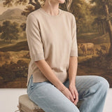 A model wearing a graced oatmeal short sleeve knit top with a crew neckline and ribbed trim, paired with light jeans.