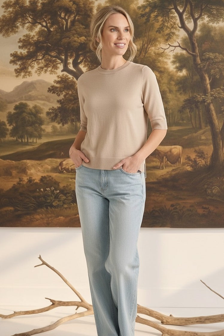 Model wearing a graced oatmeal short sleeve knit top with a crew neck and light wash jeans in a studio setting.