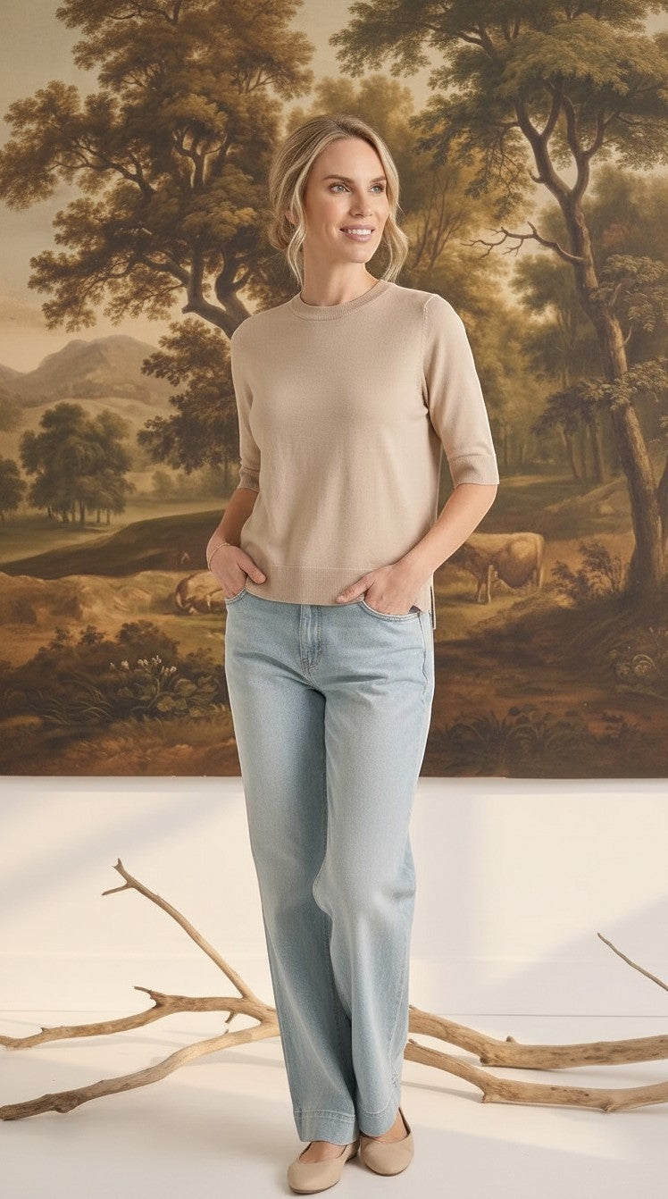 Model wearing a graced oatmeal short sleeve knit top with a crew neck and light wash jeans in a studio setting.