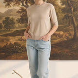 Model wearing a graced oatmeal short sleeve knit top with a crew neck and light wash jeans in a studio setting.