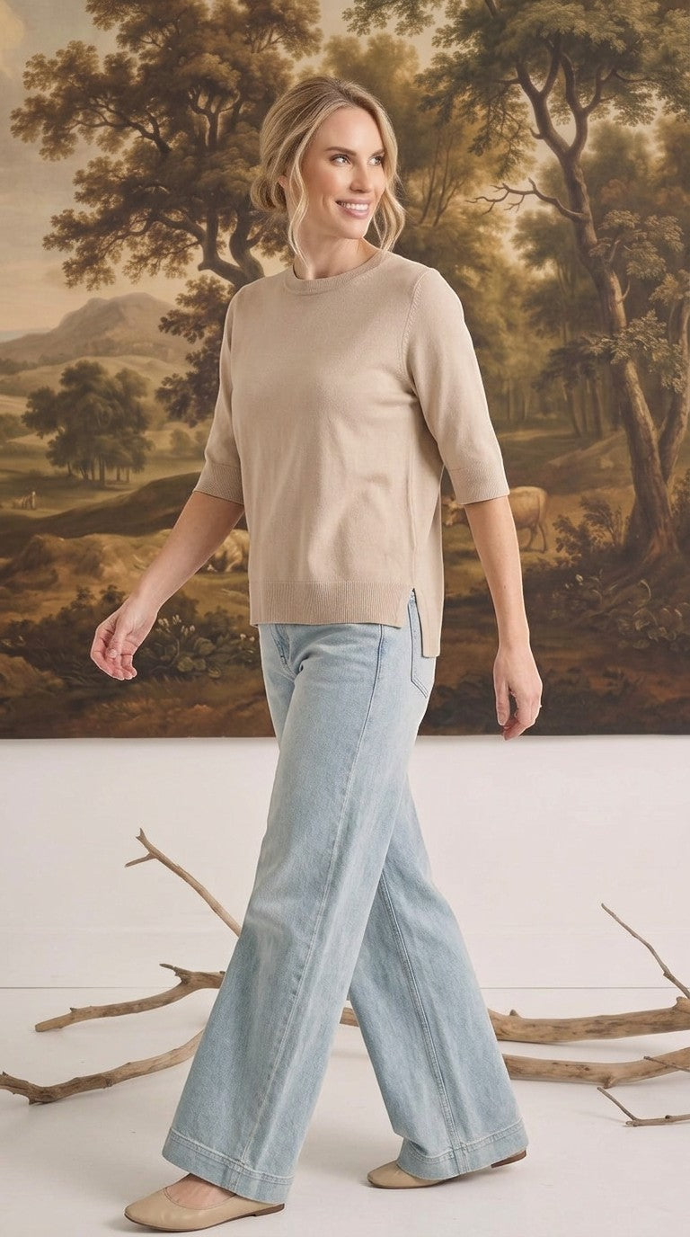 Model wearing a graced oatmeal short sleeve knit top with a crew neck and side slits, paired with light wash jeans.