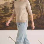 Model wearing a graced oatmeal short sleeve knit top with a crew neck and side slits, paired with light wash jeans.