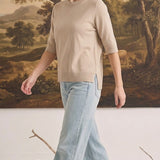 Model wearing a graced oatmeal short sleeve knit top with a crew neck and side slits, paired with light wash jeans.