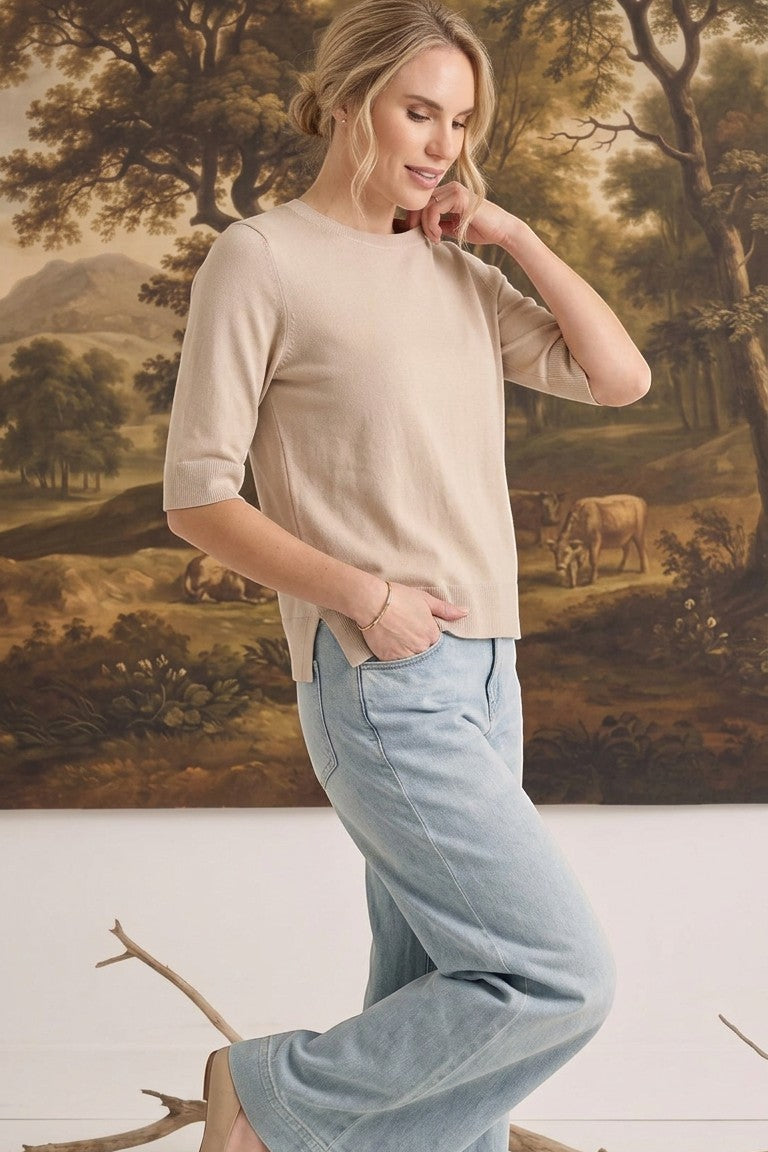 graced oatmeal short sleeve knit top worn by a woman with light blue jeans in a studio setting