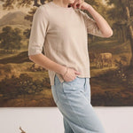 graced oatmeal short sleeve knit top worn by a woman with light blue jeans in a studio setting