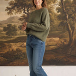graced chunky olive green crewneck sweater worn by a woman with blue jeans and white sneakers