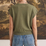 Back view of a woman wearing a graced olive green sleeveless cotton button-down top paired with blue jeans.