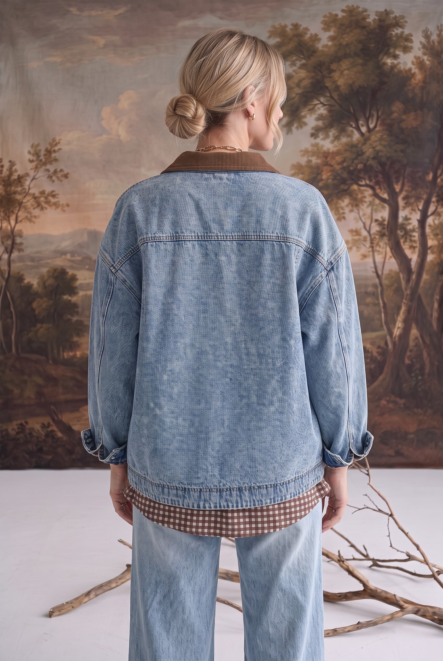Back view of a woman wearing a graced oversized blue denim jacket with a brown corduroy collar and latch hook closure