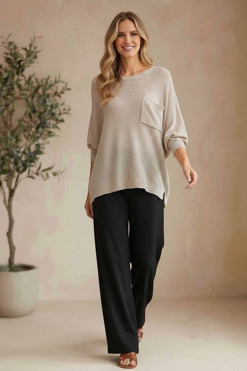 Model wearing a graced pebble dolman long sleeve knit sweater with a chest pocket and black trousers in a studio.