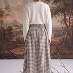 Back view of a model wearing the graced Beatrice plaid cotton midi skirt with a smocked waist and cream sweater.