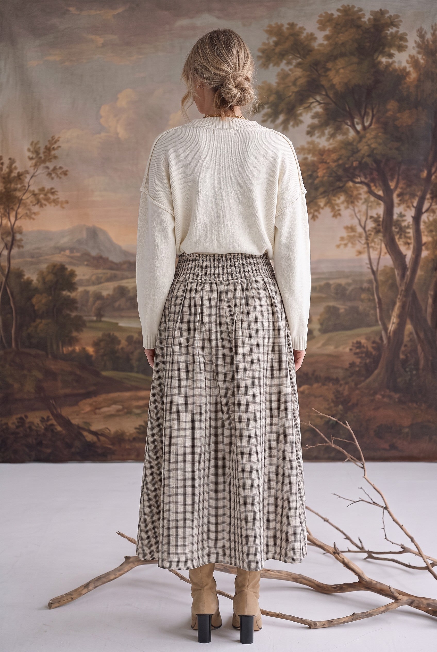 Back view of a model wearing the graced Beatrice plaid cotton midi skirt with a smocked waist and cream sweater.