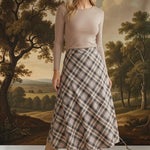 Model wearing a graced A-line midi skirt in a beige and brown plaid pattern with a long-sleeve top and suede boots.