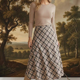 Model wearing a graced A-line midi skirt in a beige and brown plaid pattern with a long-sleeve top and suede boots.