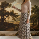 A model wearing a graced A-line midi skirt with a beige and black plaid pattern, paired with a long-sleeve top.