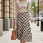 A model wearing a graced A-line midi skirt with a beige and black plaid pattern, paired with a long-sleeve top.