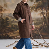 graced The Raven midi trench coat in brown with a classic collar and plaid lining, worn by a model with blue jeans.