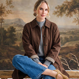 graced The Raven midi trench coat in brown with a classic collar and plaid lining, worn by a woman on a wooden bench.