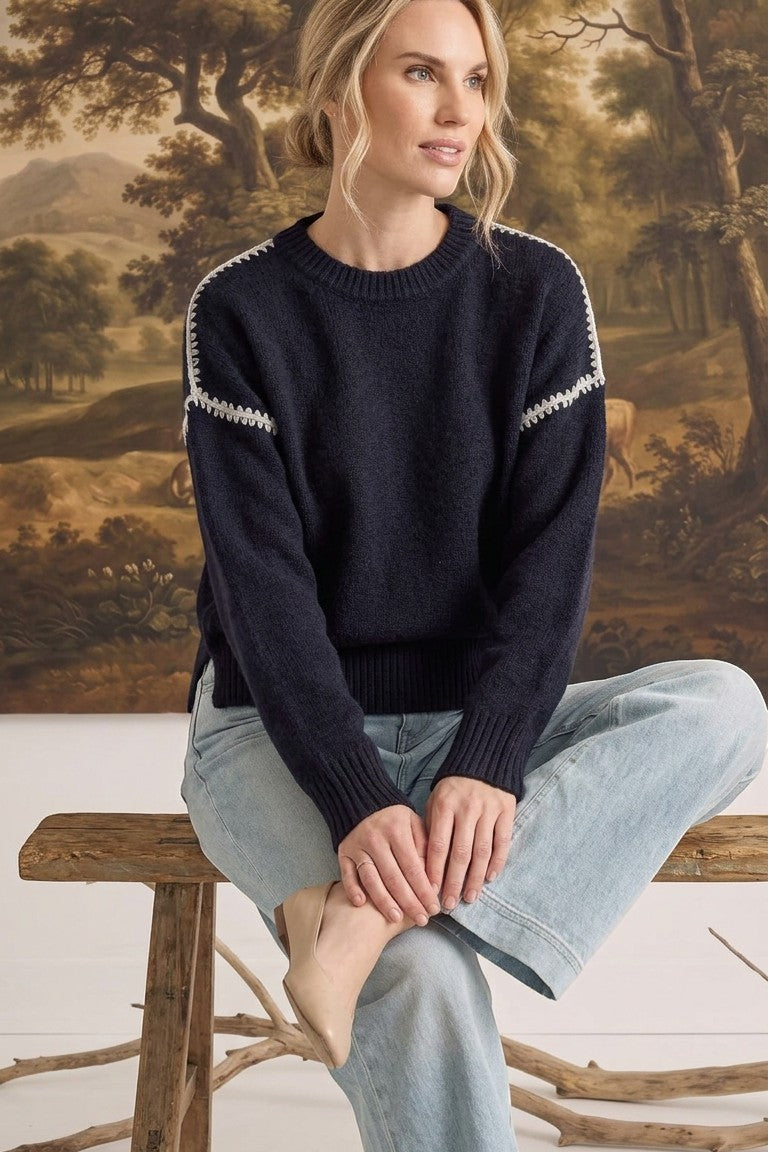 graced The Sheila Sweater in navy blue with white crochet shoulder detailing, worn by a model with light jeans.