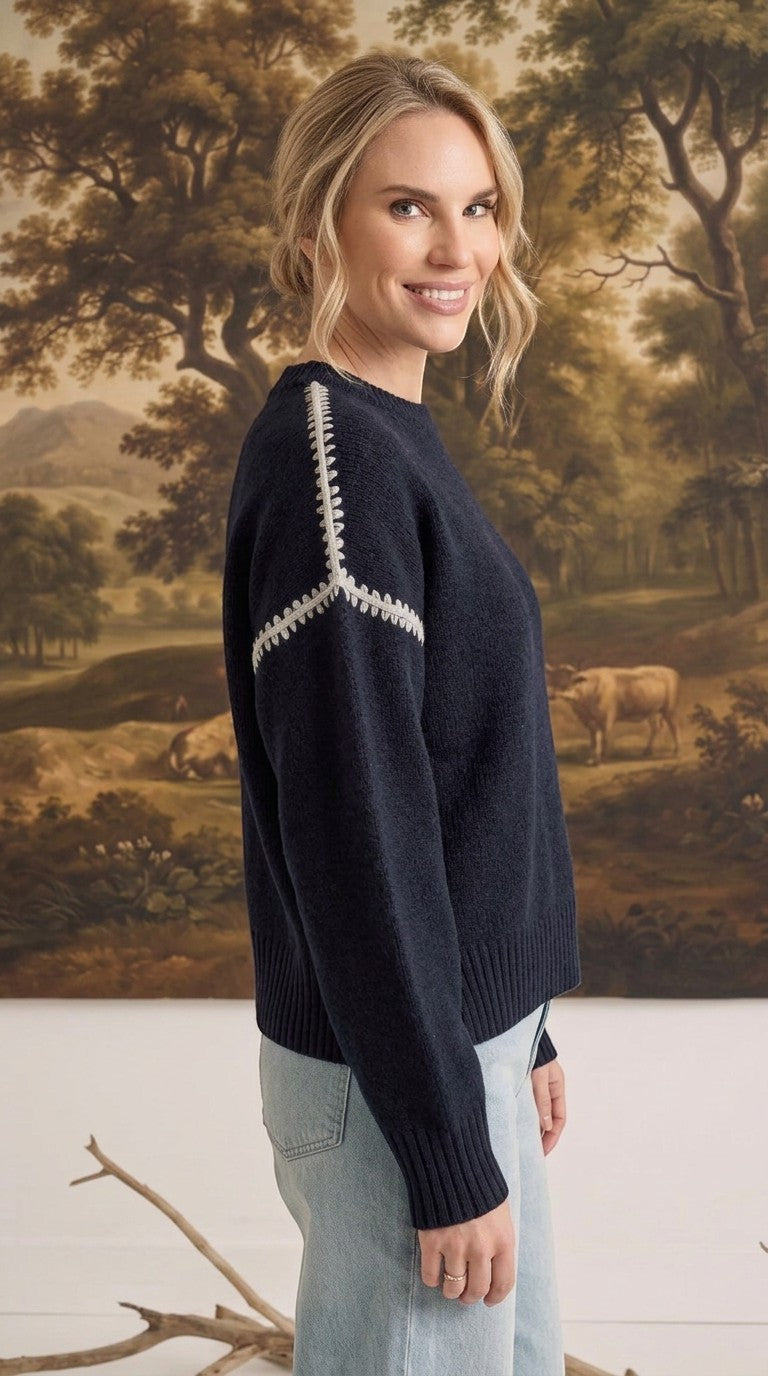 graced The Sheila Sweater in navy blue with white decorative shoulder stitching worn by a model in a side profile view