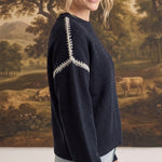 graced The Sheila Sweater in navy blue with white decorative shoulder stitching worn by a model in a side profile view