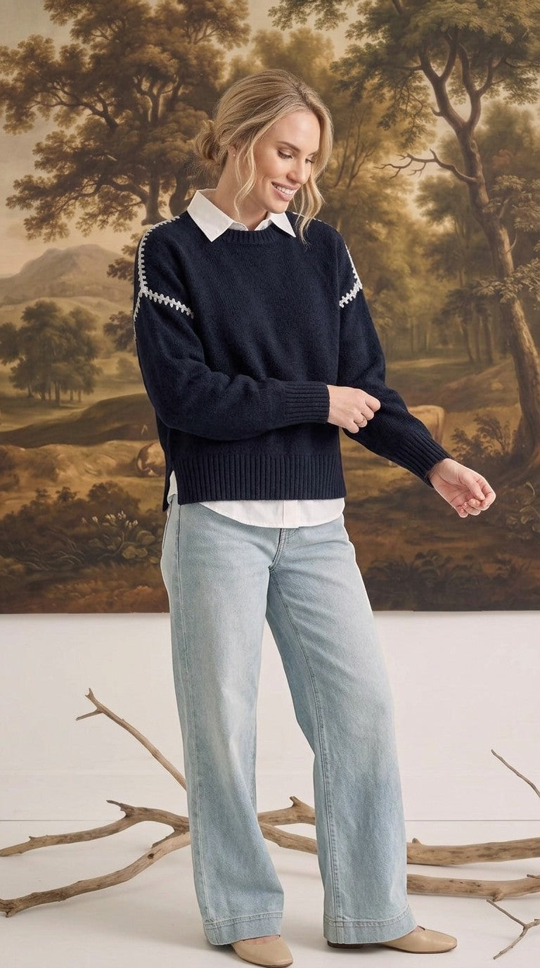 graced The Sheila Sweater in navy blue with white shoulder stitching, worn over a white shirt and light wash jeans