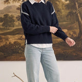 graced The Sheila Sweater in navy blue with white shoulder stitching, worn over a white shirt and light wash jeans
