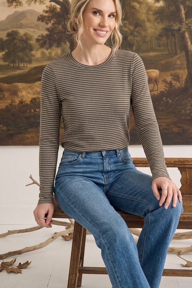 A woman wearing a graced olive and white horizontal striped long sleeve top tucked into blue denim jeans.