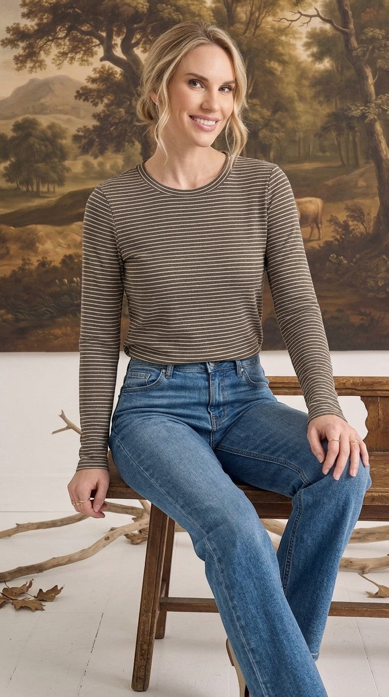 A woman wearing a graced olive and white horizontal striped long sleeve top tucked into blue denim jeans.