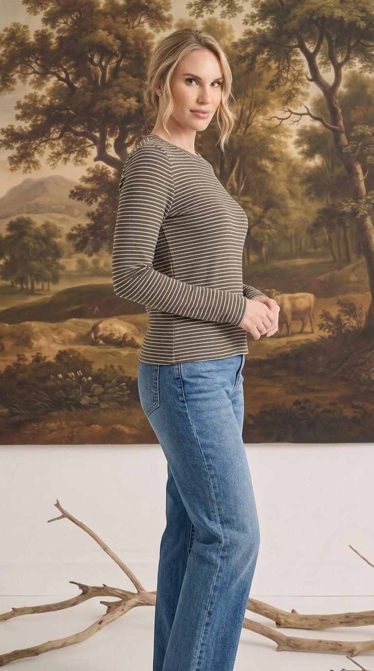 A woman wearing a graced long sleeve top with brown and white horizontal stripes, paired with blue denim jeans.