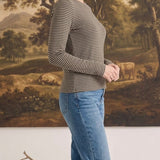A woman wearing a graced long sleeve top with brown and white horizontal stripes, paired with blue denim jeans.