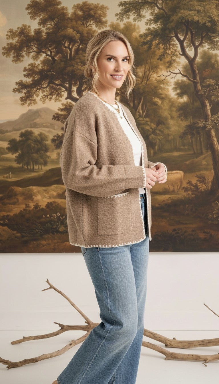Model wearing a graced tan open-front cardigan with white contrast stitching and pockets over a white top and jeans.