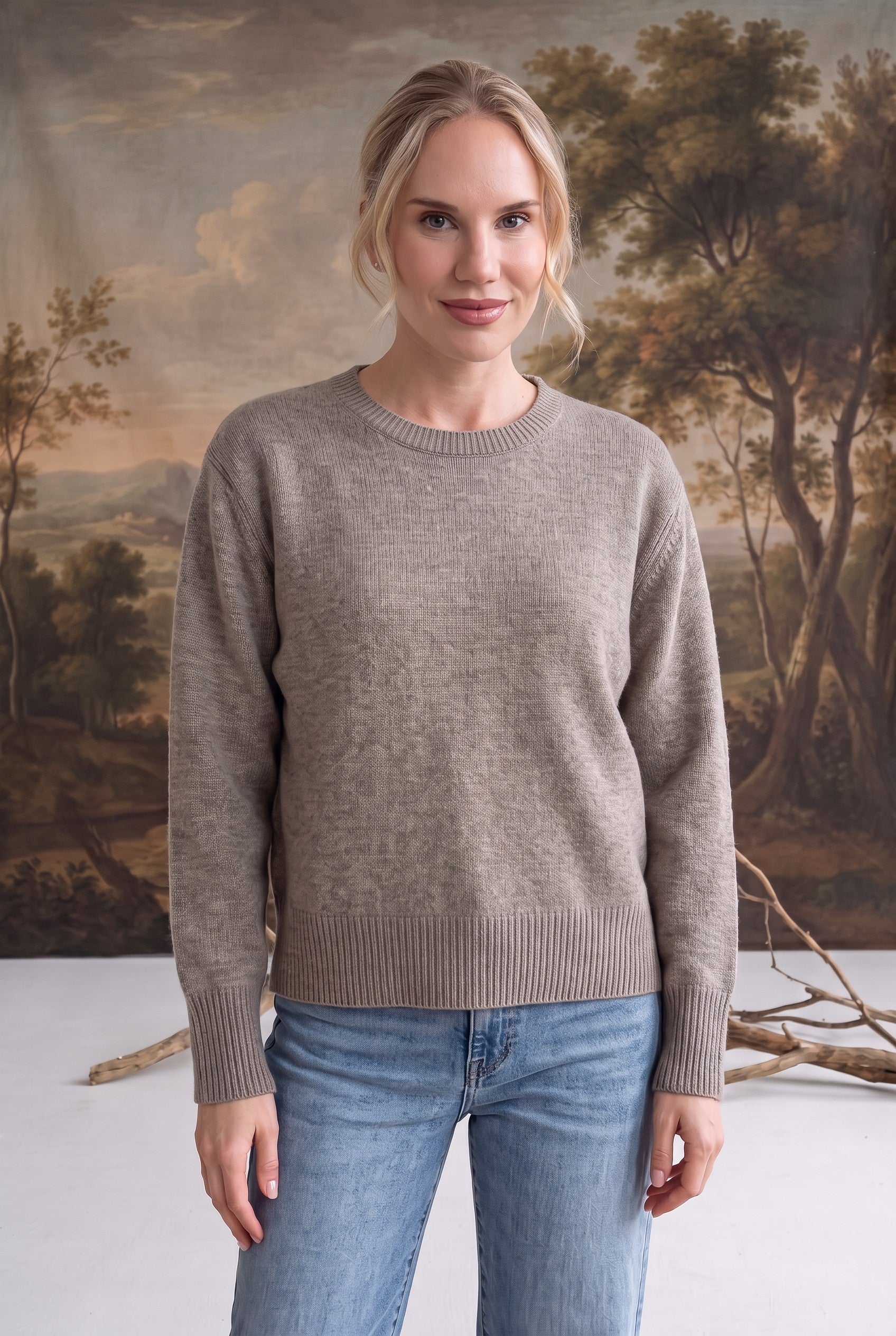 Woman wearing a graced taupe crew neck sweater with ribbed cuffs and hem, styled with blue jeans.