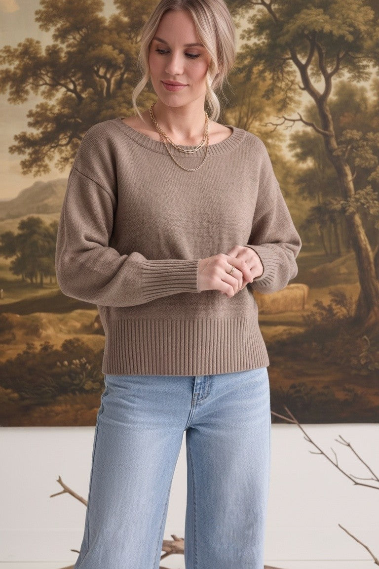 Woman wearing a graced taupe crew neck sweater with drop shoulders and wide ribbed hem paired with light wash jeans.