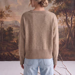 Back view of a woman wearing a graced taupe crew neck sweater with ribbed hem and cuffs, styled with light blue jeans.