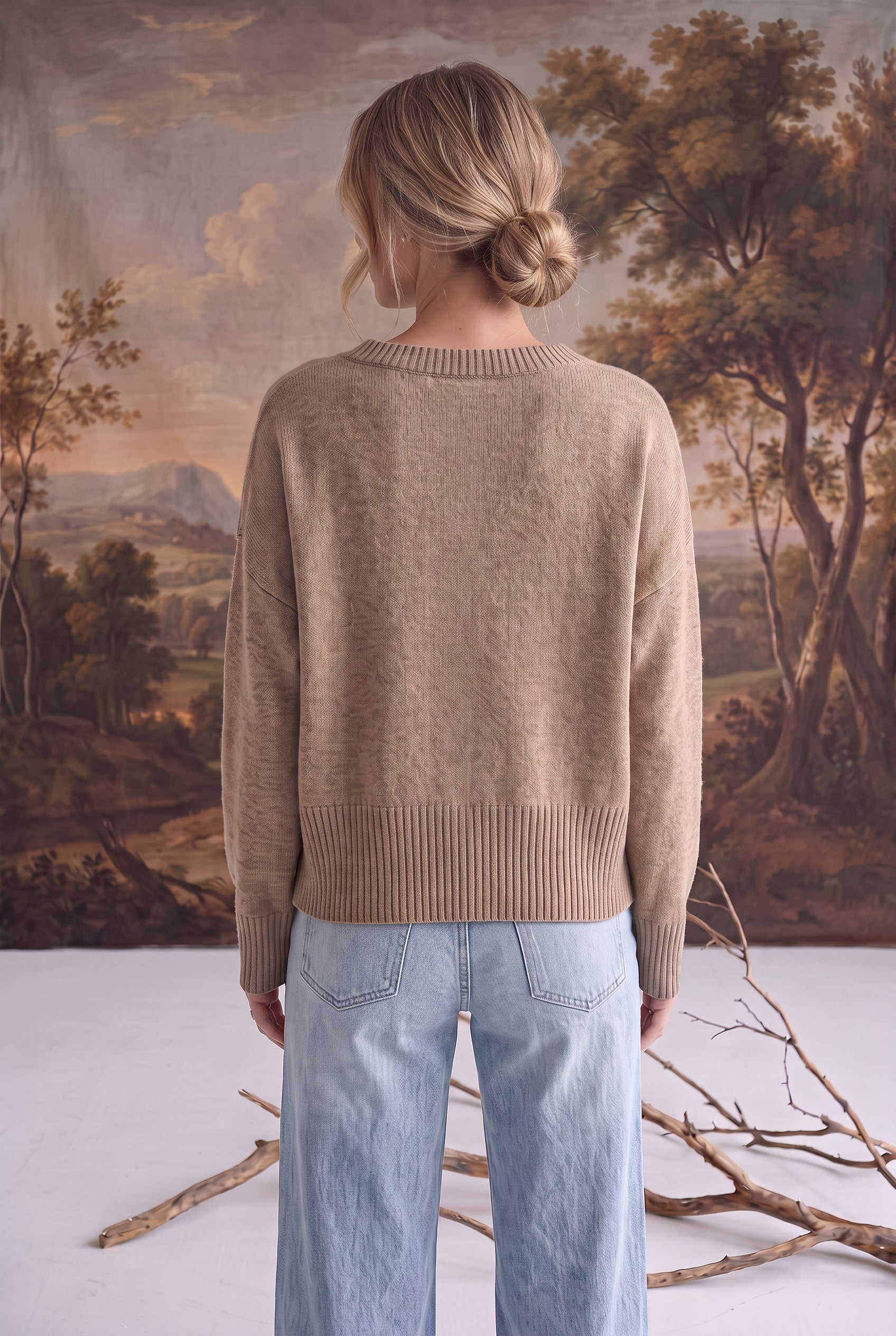 Back view of a woman wearing a graced taupe crew neck sweater with ribbed hem and cuffs, styled with light blue jeans.
