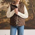 graced The Teagan Quilted Vest in brown with a floral pattern, worn over a cream sweater and blue jeans