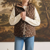 graced The Teagan Quilted Vest in brown with a floral pattern, worn over a cream sweater and blue jeans
