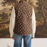 graced The Teagan Quilted Vest in brown with a floral pattern, worn over a cream sweater and blue jeans, back view