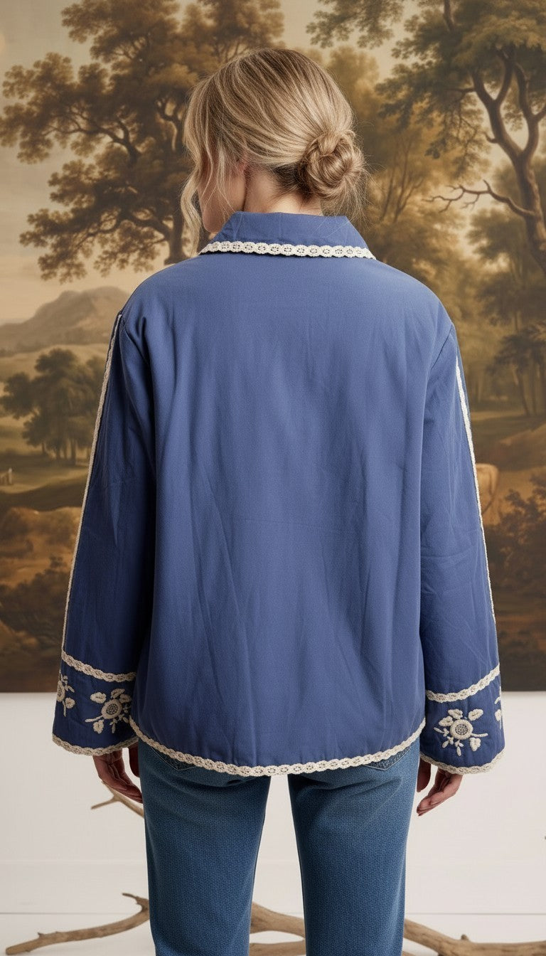 Back view of a woman wearing the blue graced The Lea Embroidered Lace Jacket with white floral embroidery details.