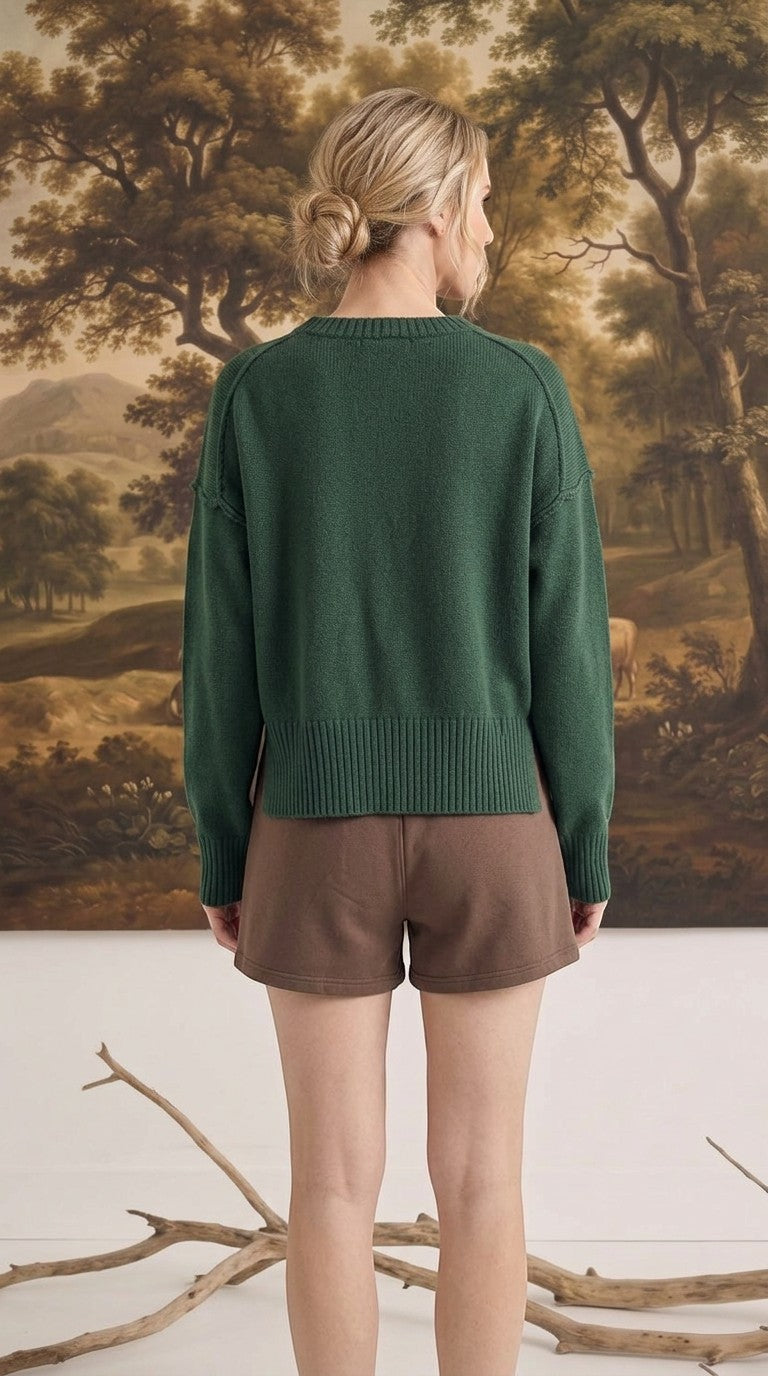 graced The Sydney Retriever Sweater in dark green with a ribbed hem and cuffs, worn by a model from the back view.