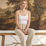 graced model wearing a white fitted spaghetti strap cami with beige jeans, sitting on a wooden bench