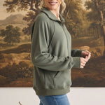 A woman wearing a graced olive green half zip mock neck pullover with long sleeves and side pockets.