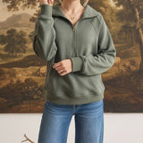 A woman wearing a graced olive green half zip mock neck pullover with long sleeves and blue denim jeans.