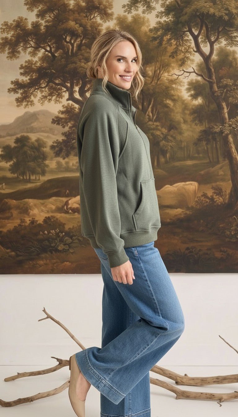 graced olive green half zip mock neck pullover worn by a woman with blue jeans in a studio setting