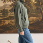 graced olive green half zip mock neck pullover worn by a woman with blue jeans in a studio setting